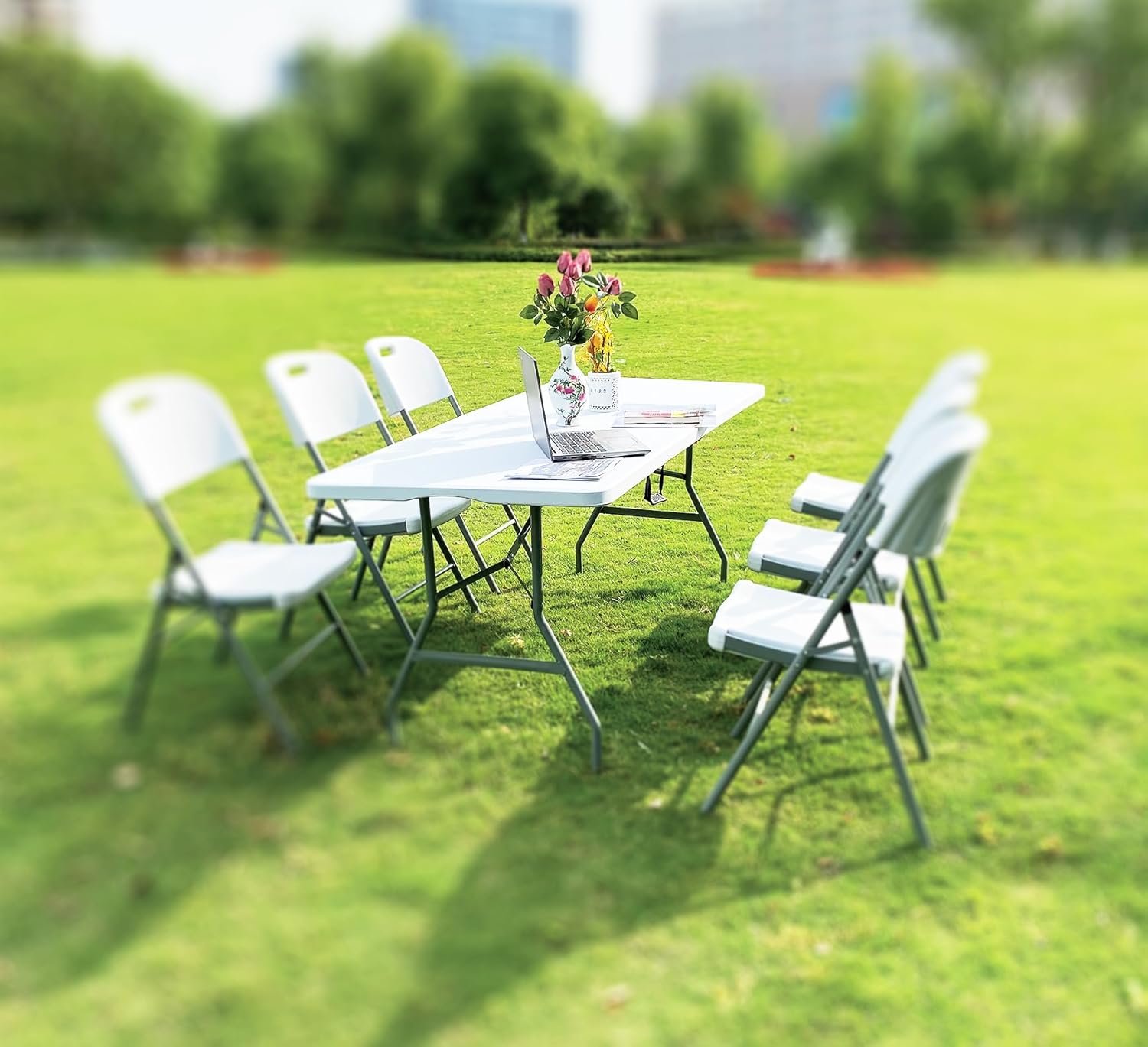 Marcolo folding white table and six chairs set up on green grass.