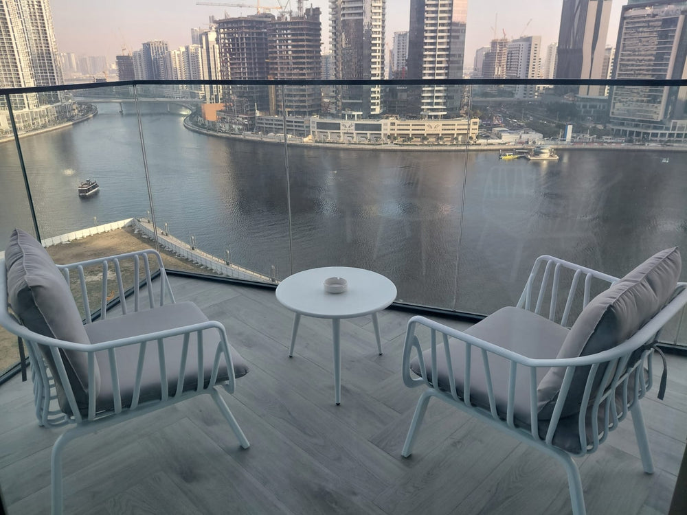 White metal lounge chairs with grey cushions on a high-rise balcony overlooking the water in Dubai