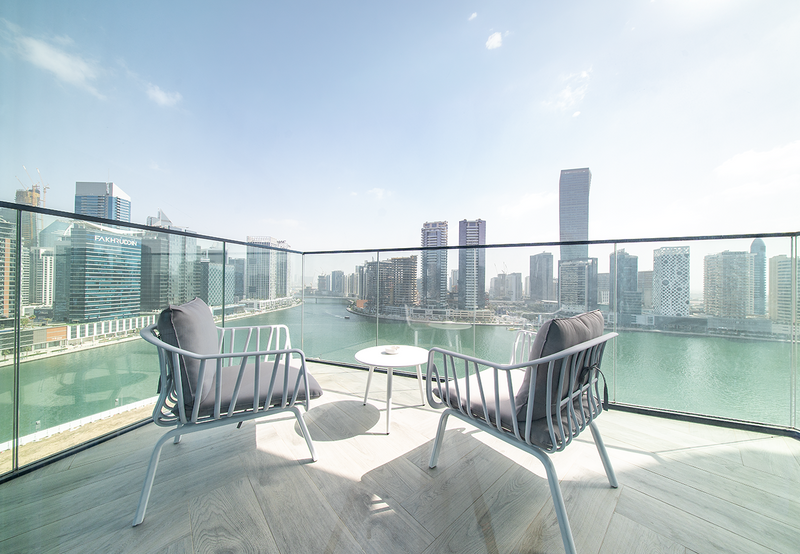 Marcolo white outdoor chairs with grey cushions on a city balcony.