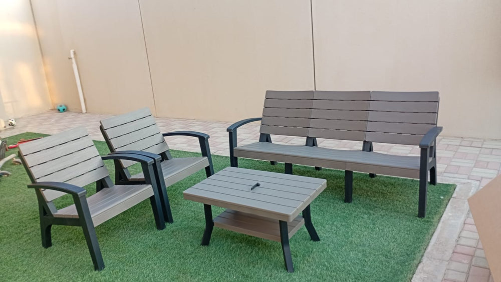 Grey slatted wood-look outdoor sofa set on artificial grass beside a villa wall