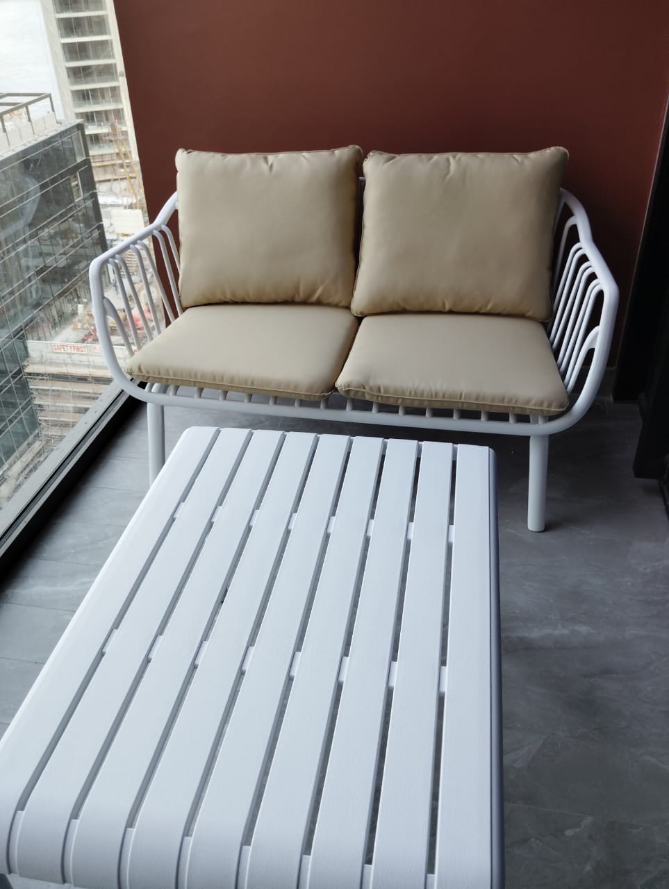 Customer's white metal loveseat with beige cushions and a slatted coffee table on a balcony